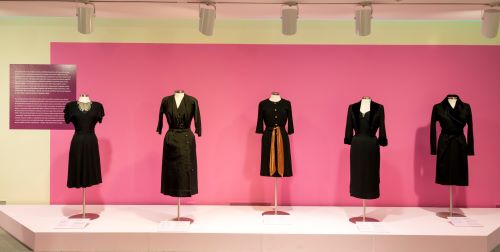 A number of iconic little black dresses lined up on forms in a display.