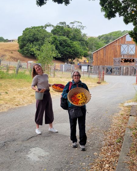 Dr. Kelsie Doty and Melody who posing on a road holding baskets of florals and other natural materials