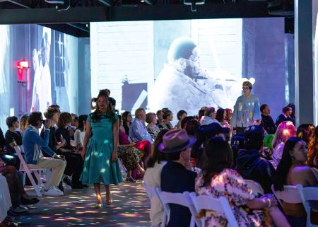 Student Model walking in a seated audience with digital imagery in the background
