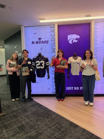 Students posing in front of a display of K-State direct product at a business site.