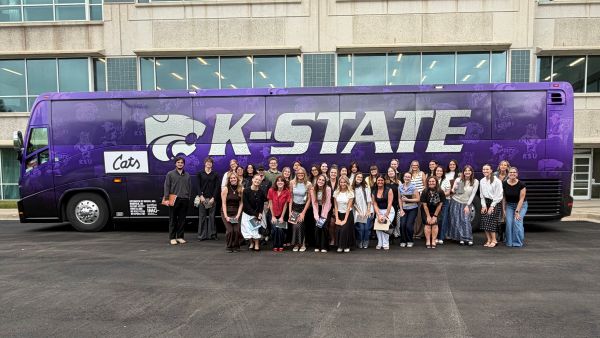 Students and instructors posing in a large group in front of the K-State vinyl covered bus that transported them to KC.