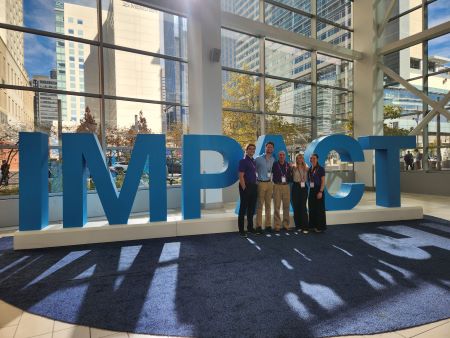 Students and instructor lined up infront of a giant sign the reads IMPACT at the Schwab IMPACT Conference in Arizona