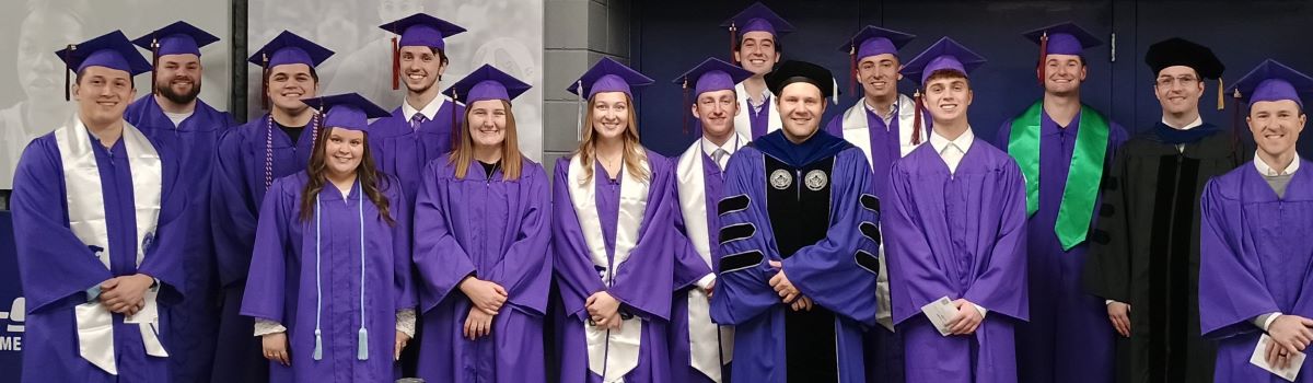 Fall 2025 Undergraduate Graduation Group Image Thirteen undergraduates lined up in their purple cap and gowns with Dr. Derek Lawson and Dr. Blake Gray at graduation