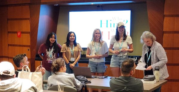 Katie Dinkel and Leah Meek standing with several others in a boardroom placing during competition