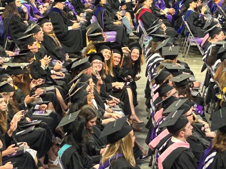 Students sitting at graduation in cap and gown in their assigned lines.