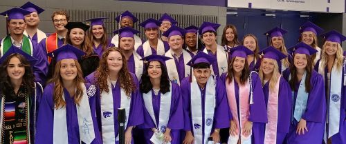 The graduating class posed together at graudation in their cap and gown with nuetral background.