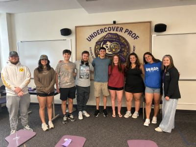 Students in Hm 650 posing in front of the Undercover Prof banner in a classroom