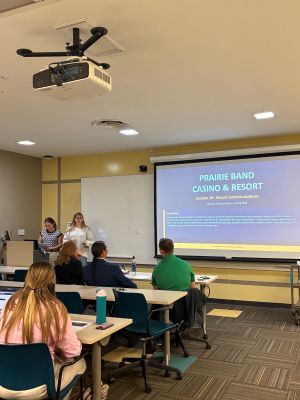 Student presenting to the Prairie Band Casino and Resort administrators in a classroom setting with slideshow background