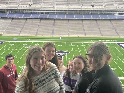 Students in HM 423 posing at Synder Stadium with the green football field and powercat as their background