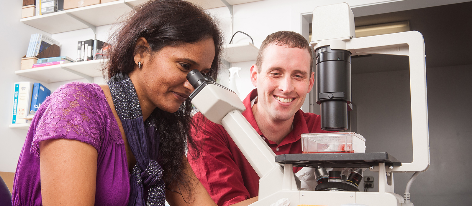Professor with student who is looking into a microscope